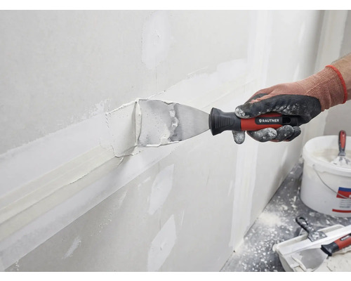 Een persoon plamuurt een muur met plamuur en een plamuurmes van Rautner.