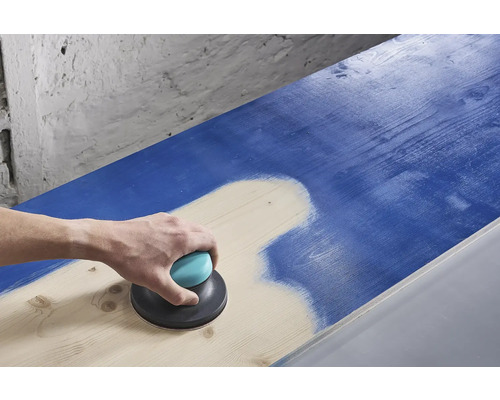 Een persoon schuurt een blauw houten oppervlak met een excentrische schuurmachine.