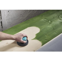 Iemand schuurt een groen geverfd houten oppervlak met een excentrische schuurmachine.