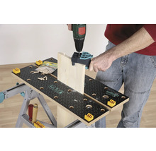 Een persoon boort een houten plank met een boormachine op een werkbank.