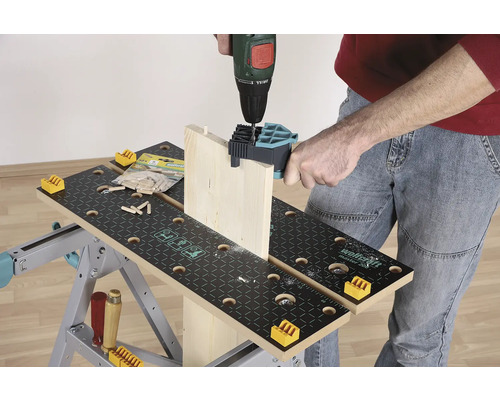 Een persoon boort een houten plank met een boormachine op een werkbank.