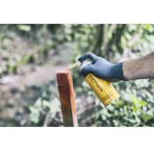 Een persoon spuit een houten paal met een gele universele spuitbus