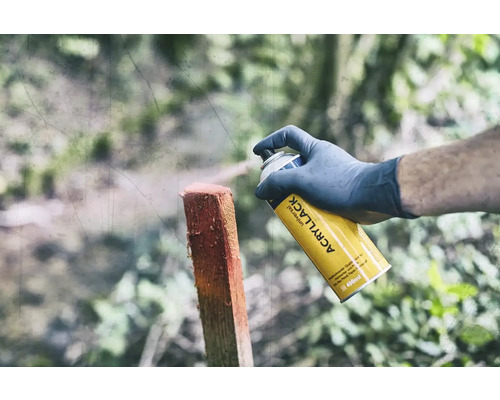 Een persoon spuit een houten paal met een gele universele spuitbus