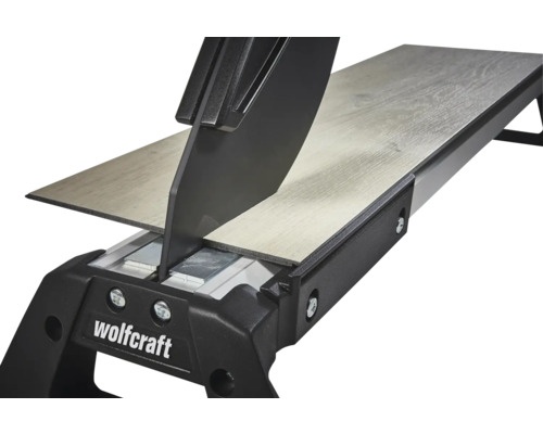 Wolfcraft laminaatsnijder snijdt een laminaatplank met houtstructuur. Detailweergave van het snijmechanisme.