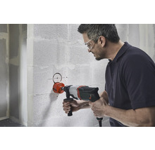 Een man boort met een gatenzaag een gat in een muur.