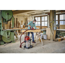 Werkplaats met vakman, schuurmachine, houten balk, werkbank, industriële stofzuiger en lintzaag