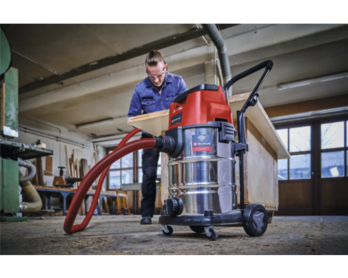 Werkplaatsopname met een Einhell nat-droogzuiger en een man die een houten plank bewerkt
