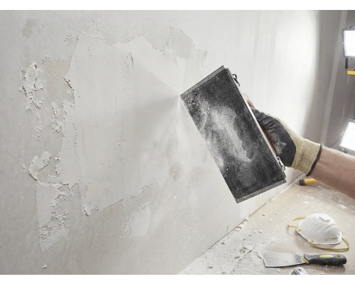 Ambachtsman schuurt muur met schuurwerktuig. Doe-het-zelfproject voor muurrenovatie.