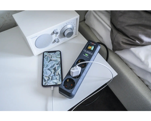 Verlengsnoer met overspanningsbeveiliging en aangesloten telefoon op een nachtkastje