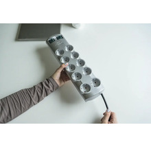 Een persoon houdt een grijs stekkerblok met tien stopcontacten vast.