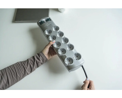 Een persoon houdt een grijs stekkerblok met tien stopcontacten vast.