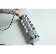 Persoon steekt stekker in een grijze stekkerdoos met tien stopcontacten