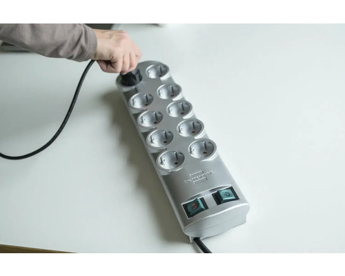 Persoon steekt stekker in een grijze stekkerdoos met tien stopcontacten