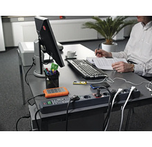 Werkplek met stekkerdoos, elektronische apparaten en persoon