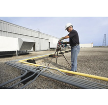 Een man in werkkleding zaagt buizen op een dak met een pijpenzaag.