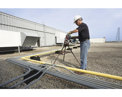 Een man in werkkleding zaagt buizen op een dak met een pijpenzaag.
