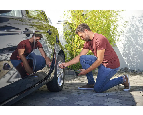 Een man controleert de bandenspanning van een auto met een bandenspanningsmeter.
