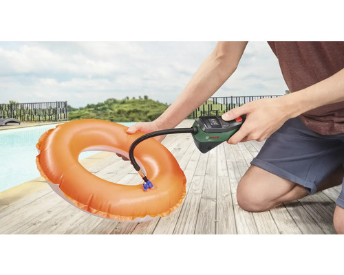 Een persoon pompt een zwemband op met een Bosch luchtpomp naast een zwembad.