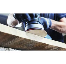 Iemand schuurt een houten plank met een excentrische schuurmachine.