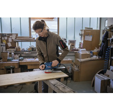 Een persoon schuurt een houten plank met een excentrische schuurmachine in een werkplaats.