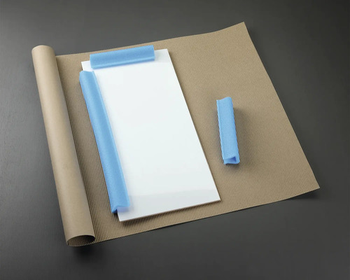 Verpakkingsmaterialen: glasplaat, papierrol, golfkarton en schuimbescherming.