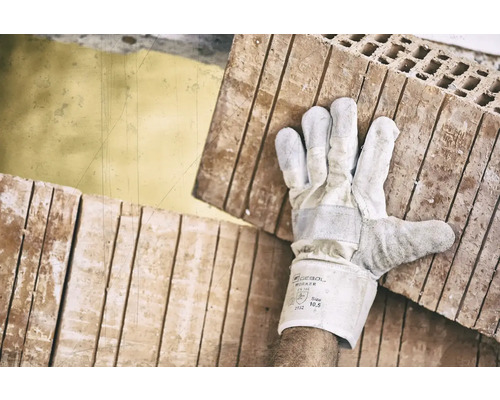 Een arbeider draagt bakstenen met handschoenen.