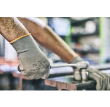 Een persoon draagt beschermende handschoenen en gebruikt een moersleutel.