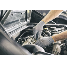 Een monteur die met beschermende handschoenen aan een automotor werkt.