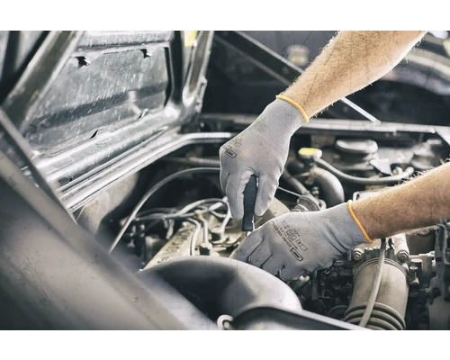 Een monteur die met beschermende handschoenen aan een automotor werkt.