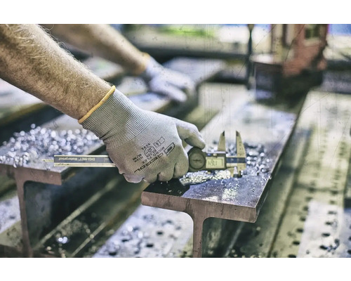 Een persoon meet een stuk metaal met een digitale schuifmaat op een ligger.