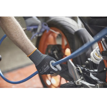 Iemand houdt een blauwe slang vast met een paar werkhandschoenen en maakt een motorfiets schoon.