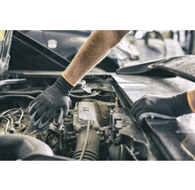 Een persoon met beschermende handschoenen werkt aan een automotor.