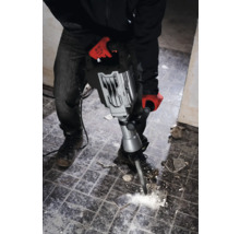 Een man met werkhandschoenen gebruikt een breekhamer om tegels te verwijderen.