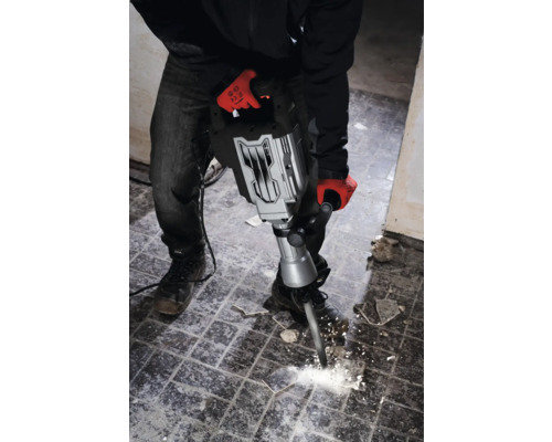 Een man met werkhandschoenen gebruikt een breekhamer om tegels te verwijderen.