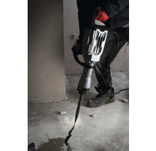 Een man gebruikt een sloophamer om een scheur in een betonnen vloer te slaan.