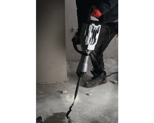 Een man gebruikt een sloophamer om een scheur in een betonnen vloer te slaan.