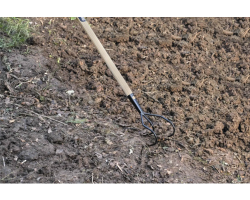 Drietandige tuinkrabber met houten handvat in de tuinbodem