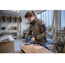 Vrouw schuurt houten plank met excentrische schuurmachine in werkplaats