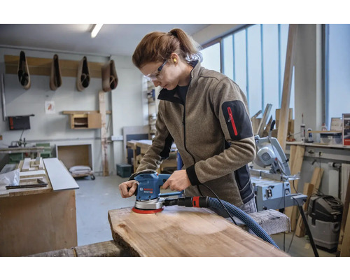Vrouw schuurt houten plank met excentrische schuurmachine in werkplaats