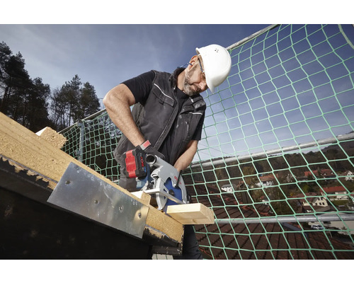Vakman met witte helm snijdt hout op een dak met een Bosch accu-cirkelzaag bij een veiligheidsnet.