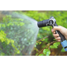 Een hand houdt een tuinspuit vast die water op planten spuit