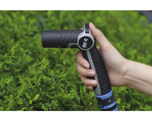 Een hand houdt een tuinspuit van het merk For Q vast voor een groene struik