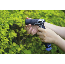 Een persoon houdt een for_q tuinspuit vast voor een groene struik.