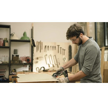 Een man zaagt een houten plank met een handcirkelzaag. Hij draagt een veiligheidsbril en handschoenen.