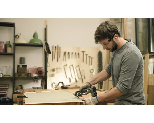 Een man zaagt een houten plank met een handcirkelzaag. Hij draagt een veiligheidsbril en handschoenen.