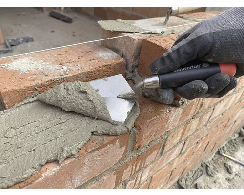 Metselaar legt baksteen met een troffel op een bouwplaats