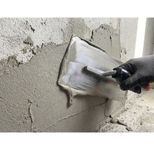 Iemand smeert gips met een pleisterspaan op een muur.