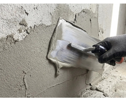 Iemand smeert gips met een pleisterspaan op een muur.