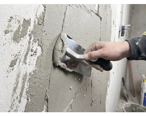 Ambachtsman brengt stuc aan op een muur met een spaan.