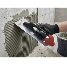 Tegellijm aanbrengen op een muur met een roestvrijstalen troffel